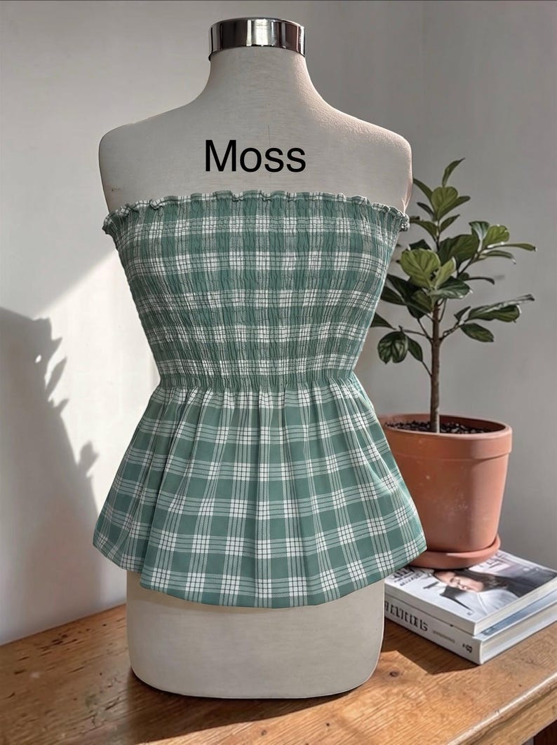 Peut inclure: Un haut bustier sans bretelles &agrave; motif &eacute;cossais vert mousse et blanc. Le v&ecirc;tement pr&eacute;sente un corsage smock&eacute; et &eacute;lastique avec un bord sup&eacute;rieur volant&eacute; et un ourlet &agrave; basque &eacute;vas&eacute;. Le mot Moss est imprim&eacute; en noir au-dessus du v&ecirc;tement.