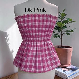 Peut inclure: Un haut bustier sans bretelles &agrave; motif &eacute;cossais rose fonc&eacute; et blanc. Le v&ecirc;tement pr&eacute;sente un corsage fronc&eacute; et &eacute;lastique avec un bord sup&eacute;rieur volant&eacute; et un ourlet &agrave; basque &eacute;vas&eacute;. Le texte 'Dk Pink' est imprim&eacute; en noir au-dessus du v&ecirc;tement.