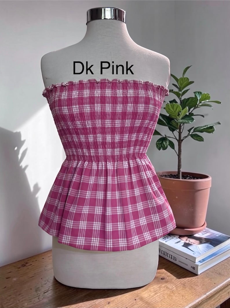 Peut inclure: Un haut bustier sans bretelles &agrave; motif &eacute;cossais rose fonc&eacute; et blanc. Le v&ecirc;tement pr&eacute;sente un corsage fronc&eacute; et &eacute;lastique avec un bord sup&eacute;rieur volant&eacute; et un ourlet &agrave; basque &eacute;vas&eacute;. Le texte 'Dk Pink' est imprim&eacute; en noir au-dessus du v&ecirc;tement.