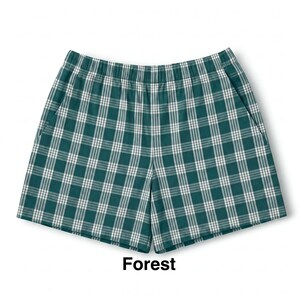 K&ouml;nnte beinhalten: Eine Shorts mit einem dunkelwaldgr&uuml;nen und wei&szlig;en Karomuster, ausgestattet mit einem breiten elastischen Bund und Seitentaschen. Das Wort Forest ist in schwarzer Schrift unter der Shorts abgedruckt und gibt die Farbe des Kleidungsst&uuml;cks an.