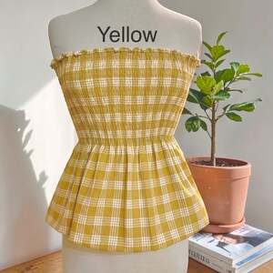 Peut inclure: Un haut bustier sans bretelles &agrave; motif &eacute;cossais jaune et blanc. Le v&ecirc;tement pr&eacute;sente un corsage smock&eacute; et &eacute;lastique avec un bord sup&eacute;rieur volant&eacute; et un ourlet &agrave; basque &eacute;vas&eacute;. Le mot Yellow est imprim&eacute; en noir au-dessus du v&ecirc;tement sur le mannequin.
