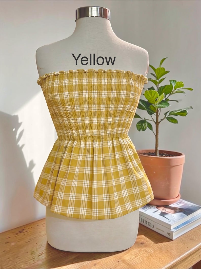 Peut inclure: Un haut bustier sans bretelles &agrave; motif &eacute;cossais jaune et blanc. Le v&ecirc;tement pr&eacute;sente un corsage smock&eacute; et &eacute;lastique avec un bord sup&eacute;rieur volant&eacute; et un ourlet &agrave; basque &eacute;vas&eacute;. Le mot Yellow est imprim&eacute; en noir au-dessus du v&ecirc;tement sur le mannequin.