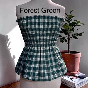 Peut inclure: Un haut bustier sans bretelles avec un motif &agrave; carreaux vert for&ecirc;t et blanc. Le v&ecirc;tement pr&eacute;sente un corsage smock&eacute; et &eacute;lastique avec un bord sup&eacute;rieur volant&eacute; et un ourlet &agrave; basque &eacute;vas&eacute;. Le texte Forest Green est imprim&eacute; au-dessus.