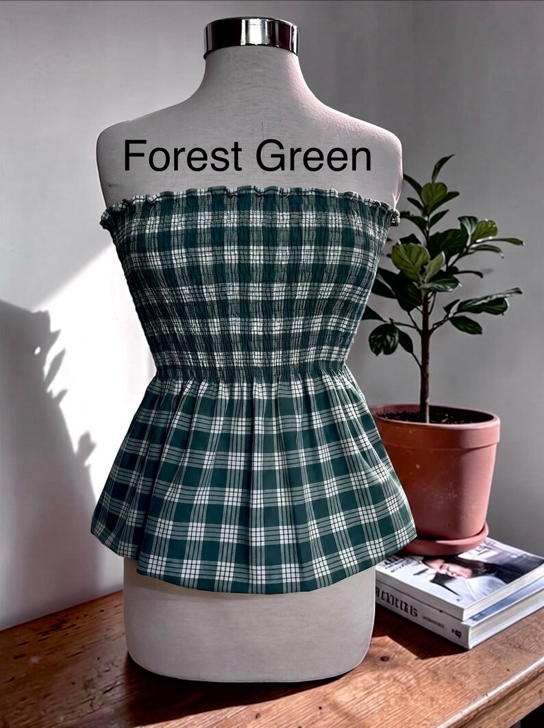Peut inclure: Un haut bustier sans bretelles avec un motif &agrave; carreaux vert for&ecirc;t et blanc. Le v&ecirc;tement pr&eacute;sente un corsage smock&eacute; et &eacute;lastique avec un bord sup&eacute;rieur volant&eacute; et un ourlet &agrave; basque &eacute;vas&eacute;. Le texte Forest Green est imprim&eacute; au-dessus.