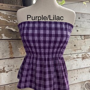 May include: A strapless tube top featuring a purple and white plaid pattern with a smocked bodice and a flared peplum hem. The text "Purple/Lilac" is printed above the garment on the mannequin.