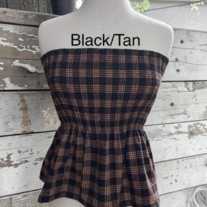 May include: A strapless tube top featuring a black and tan plaid pattern with a smocked bodice and a flared peplum hem. The text Black/Tan is printed above the garment on the mannequin.