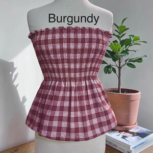 Peut inclure: Un haut bustier sans bretelles &agrave; motif &eacute;cossais bordeaux et blanc. Le v&ecirc;tement pr&eacute;sente un corsage smock&eacute; et &eacute;lastique avec un bord sup&eacute;rieur volant&eacute; et un ourlet &agrave; basque &eacute;vas&eacute;. Le mot Burgundy est imprim&eacute; en noir au-dessus du haut.