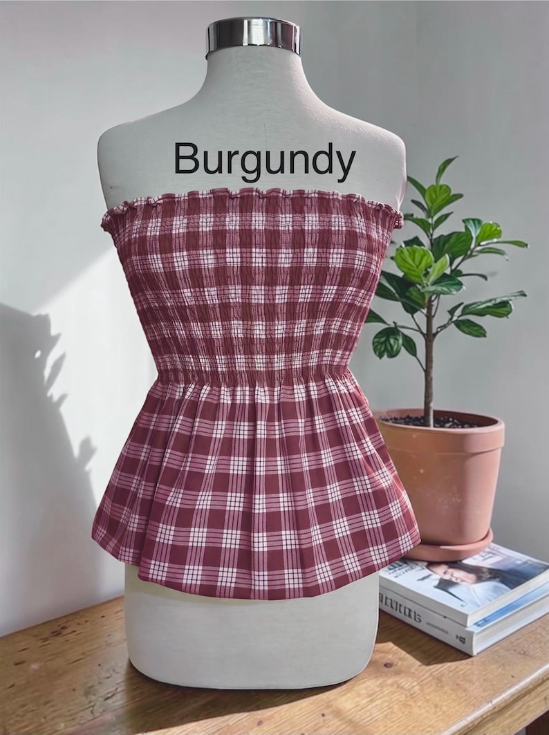 Peut inclure: Un haut bustier sans bretelles &agrave; motif &eacute;cossais bordeaux et blanc. Le v&ecirc;tement pr&eacute;sente un corsage smock&eacute; et &eacute;lastique avec un bord sup&eacute;rieur volant&eacute; et un ourlet &agrave; basque &eacute;vas&eacute;. Le mot Burgundy est imprim&eacute; en noir au-dessus du haut.
