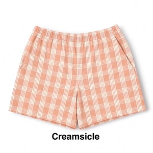 K&ouml;nnte beinhalten: Eine Shorts mit pfirsichfarbenem und wei&szlig;em Karomuster, ausgestattet mit einem elastischen Bund und zwei Seitentaschen. Der Text Creamsicle ist in Schwarz unter dem Kleidungsst&uuml;ck aufgedruckt und gibt die Farbgebung des Karomusters an.
