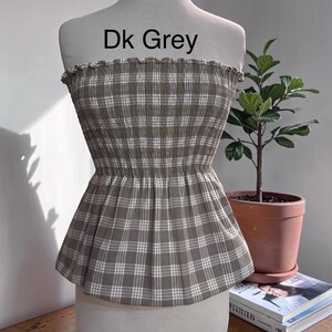 May include: A strapless tube top featuring a dark grey and white plaid pattern with a smocked, elasticized bodice and a flared peplum hem. The text Dk Grey is printed above the garment on the mannequin display.