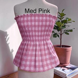Peut inclure: Un haut bustier sans bretelles &agrave; motif &eacute;cossais rose moyen et blanc. Le v&ecirc;tement pr&eacute;sente un corsage smock&eacute; et &eacute;lastique avec un bord sup&eacute;rieur volant&eacute; et un ourlet &agrave; basque &eacute;vas&eacute;. Le texte Med Pink est imprim&eacute; en noir au-dessus du v&ecirc;tement.