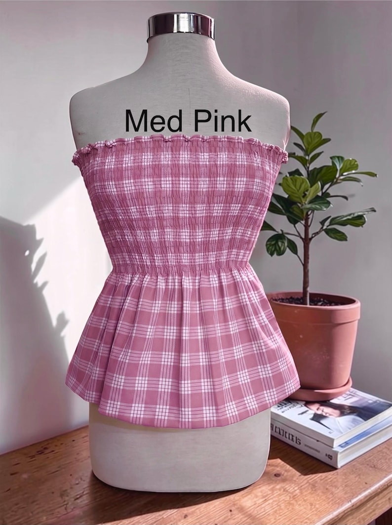 Peut inclure: Un haut bustier sans bretelles &agrave; motif &eacute;cossais rose moyen et blanc. Le v&ecirc;tement pr&eacute;sente un corsage smock&eacute; et &eacute;lastique avec un bord sup&eacute;rieur volant&eacute; et un ourlet &agrave; basque &eacute;vas&eacute;. Le texte Med Pink est imprim&eacute; en noir au-dessus du v&ecirc;tement.