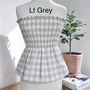 May include: A strapless tube top featuring a light grey and white plaid pattern with a smocked, elasticized bodice and a ruffled top edge. The garment is displayed on a mannequin and includes the printed text Lt Grey above the neckline.