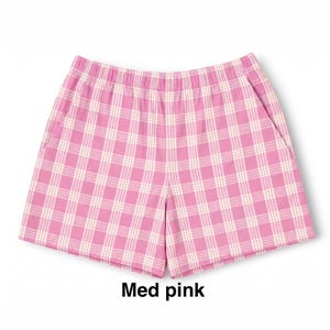 K&ouml;nnte beinhalten: Rosa-wei&szlig; karierte Shorts mit elastischem Bund und zwei Seitentaschen. Der Stoff zeigt ein durchgehendes Karomuster. Unter der Shorts ist der Text "Med pink" in schwarzer Schrift aufgedruckt.