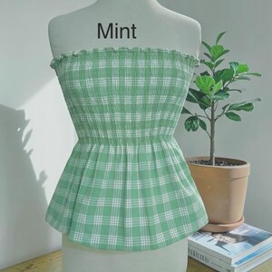 Peut inclure: Un haut bustier sans bretelles &agrave; motif &eacute;cossais vert menthe et blanc, dot&eacute; d'un corsage smock&eacute; &eacute;lastique et d'un bord sup&eacute;rieur volant&eacute;. Le mot Mint est imprim&eacute; en gris fonc&eacute; au-dessus du v&ecirc;tement sur le torse du mannequin blanc.