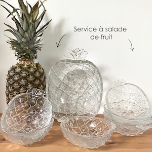 Könnte beinhalten: Ein klares, glasförmiges Ananas-Servierset, einschließlich einer großen Schüssel mit Deckel und mehreren kleineren Schalen. Das Set hat eine strukturierte Oberfläche und ist zum Servieren von Obst gedacht. Eine frische Ananas ist ebenfalls im Bild.