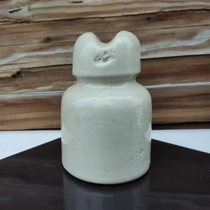 Op de afbeelding: Een witte keramische isolator met een afgeronde bovenkant en een klein gat in het midden. De isolator heeft een ruw, getextureerd oppervlak en de letters "HFC" zijn gestempeld op de bovenkant.