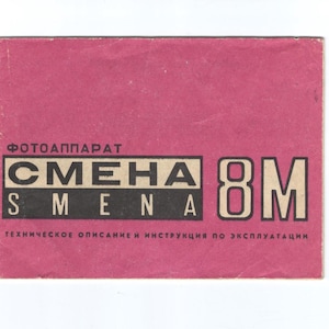 Könnte beinhalten: Ein pinkfarbenes Vintage-Handbuch für eine "SMENA 8M" Kamera. Das Cover zeigt den Namen der Kamera in schwarzen und weißen Blockbuchstaben, mit kyrillischem Text darüber und darunter. Das Handbuch ist rechteckig.