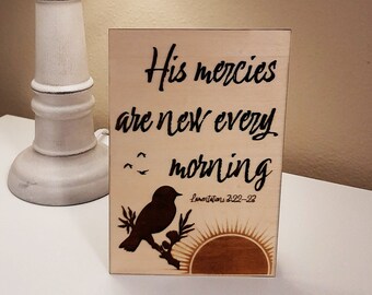May include: Wooden sign with a burnt-in design of a bird, a sunrise, and the text "His mercies are new every morning" with the scripture reference "Lamentations 3:22-23".