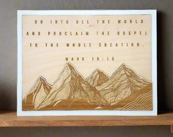 May include: A wooden sign with a white frame features a mountain range illustration and the text "Go into all the world and proclaim the gospel to the whole creation. Mark 10:15."