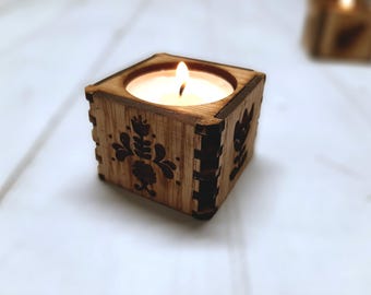May include: A wooden candle holder with a floral design. The holder is square and has a small candle inside.