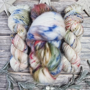 May include: A collection of colorful yarn skeins in various textures and hues, including white, blue, red, and green. The yarn is arranged on a rustic wooden surface, with decorative stars and frosted greenery.