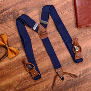 May include: Navy blue braces with brown leather accents and a personalised leather patch that reads "Kevin 11.23.2024".