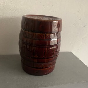 May include: A brown ceramic barrel-shaped jar with a lid. The jar has a wood grain pattern.