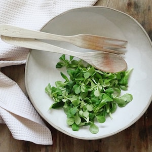 May include: A white ceramic bowl with a salad of green lettuce and two wooden spoons with the word "always" engraved on them.