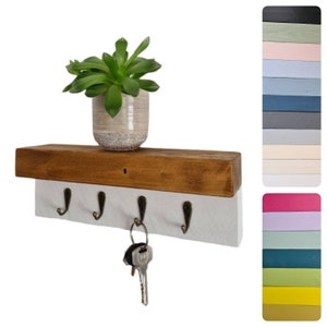 May include: A rustic wooden shelf with a white painted front, featuring five metal hooks for hanging keys. The shelf has a natural wood top and is decorated with a small potted succulent plant.