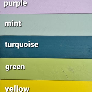 May include: A vertical image showcasing seven painted wooden planks in various colors. The colors include berry pink, purple, mint, turquoise, green, yellow, and yellow ochre. Each plank has the color name in white text.