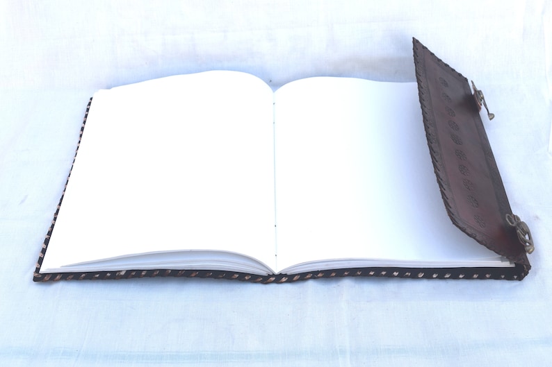 K&ouml;nnte beinhalten: Ein braunes, ledergebundenes Tagebuch mit dekorativen N&auml;hten und Metallschlie&szlig;en. Das Tagebuch ist ge&ouml;ffnet und zeigt leere wei&szlig;e Seiten.