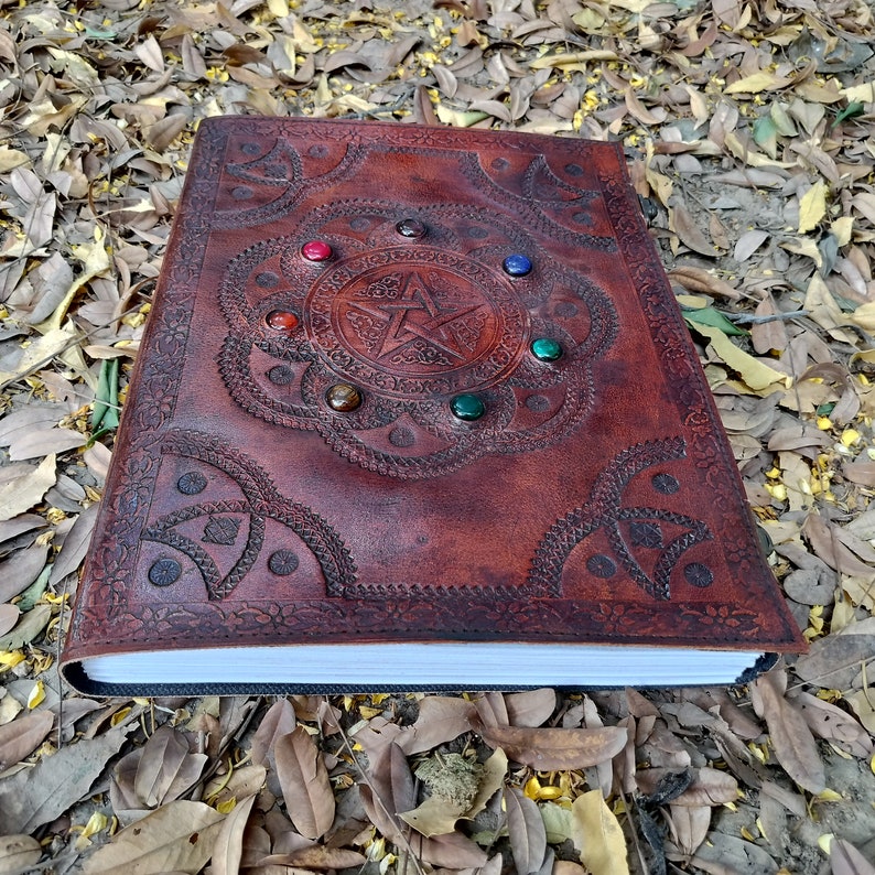 Pu&ograve; includere: Un diario in pelle marrone con un design a pentagramma e pietre preziose colorate incastonate nella copertina.