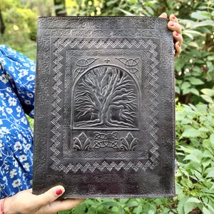 Puede incluir: Un diario de cuero negro con un dise&ntilde;o de &aacute;rbol de la vida celta en relieve. El diario tiene un borde decorativo alrededor del &aacute;rbol de la vida.