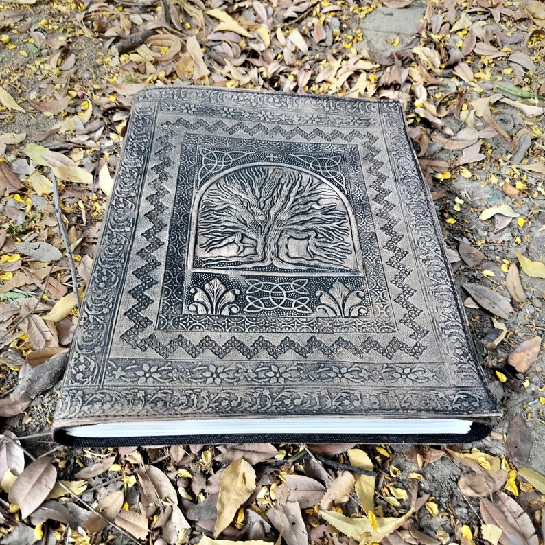 Puede incluir: Un diario de cuero negro con un dise&ntilde;o en relieve detallado de un &aacute;rbol de la vida. El diario tiene un borde de nudo celta y un marco decorativo alrededor del &aacute;rbol.