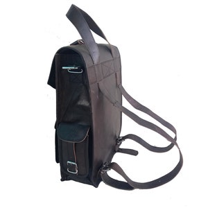 Pode incluir: Uma mochila de couro marrom com um grande bolso frontal e al&ccedil;as ajust&aacute;veis. A mochila tem uma al&ccedil;a superior e um fecho de aba.
