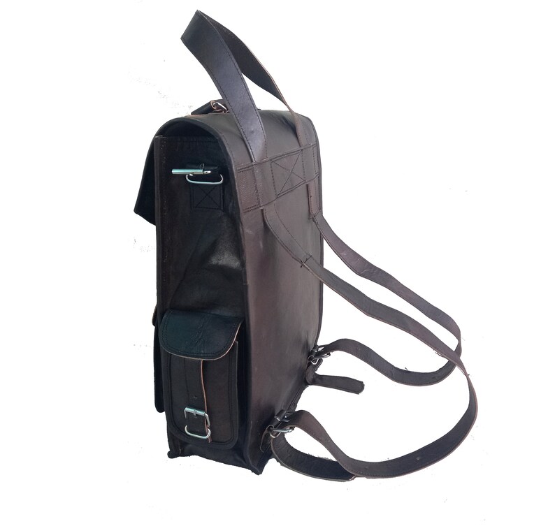 Pode incluir: Uma mochila de couro marrom com um grande bolso frontal e al&ccedil;as ajust&aacute;veis. A mochila tem uma al&ccedil;a superior e um fecho de aba.