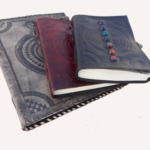 K&ouml;nnte beinhalten: Drei ledergebundene Journale mit aufwendigen Designs. Das obere Journal hat einen schwarzen Einband mit bunten Edelsteinen und einem Mandala-Muster. Das mittlere Journal hat einen burgunderfarbenen Einband mit einem &auml;hnlichen Mandala-Muster. Das untere Journal hat einen grauen Einband mit einem aufwendigeren Design.