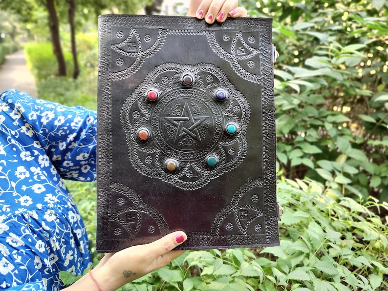 Pu&ograve; includere: Diario in pelle nera con un design a pentagramma e pietre preziose colorate attorno ai bordi. Il diario ha un motivo in rilievo decorativo.