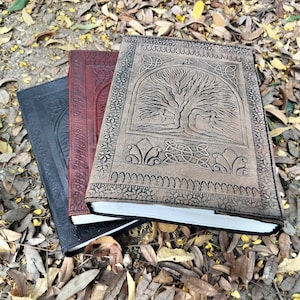 Puede incluir: Tres diarios encuadernados en cuero con dise&ntilde;os en relieve. El diario superior presenta un dise&ntilde;o de &aacute;rbol de la vida con detalles intrincados. El diario del medio es rojo y el diario inferior es negro.