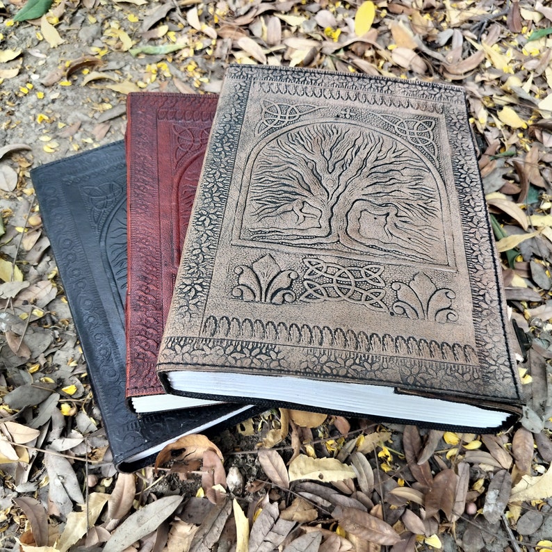 Puede incluir: Tres diarios encuadernados en cuero con dise&ntilde;os en relieve. El diario superior presenta un dise&ntilde;o de &aacute;rbol de la vida con detalles intrincados. El diario del medio es rojo y el diario inferior es negro.