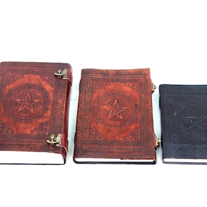 May include: Three leather-bound journals with embossed pentagram designs. The journals vary in size and color, with the largest being reddish-brown, the middle one is also reddish-brown, and the smallest is dark brown. Each has a metal clasp.