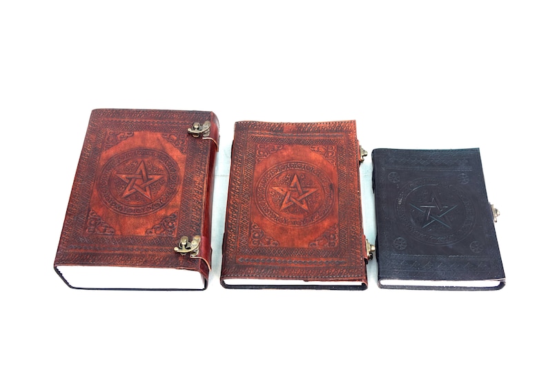 May include: Three leather-bound journals with embossed pentagram designs. The journals vary in size and color, with the largest being reddish-brown, the middle one is also reddish-brown, and the smallest is dark brown. Each has a metal clasp.