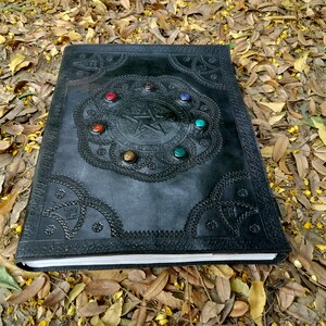 Pu&ograve; includere: Diario rilegato in pelle nera con un design a pentagramma in rilievo e pietre preziose colorate attorno ai bordi.
