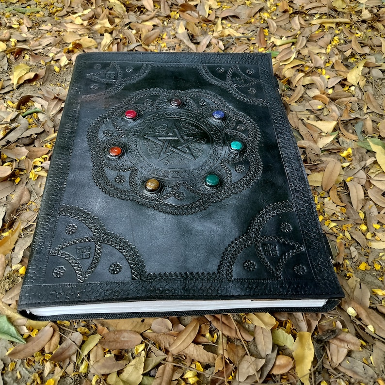 Pu&ograve; includere: Diario rilegato in pelle nera con un design a pentagramma in rilievo e pietre preziose colorate attorno ai bordi.