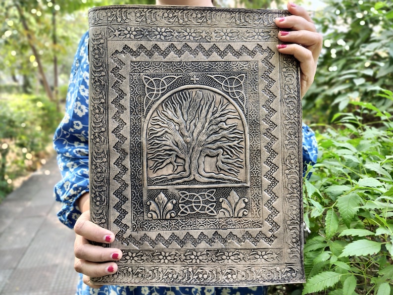 Puede incluir: Un diario de cuero marr&oacute;n con un dise&ntilde;o de &aacute;rbol de la vida en relieve. El diario tiene un borde de nudo celta y detalles intrincados.