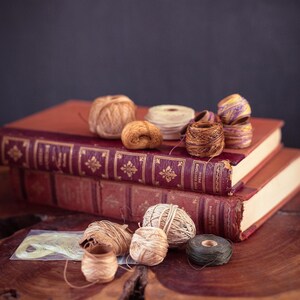 Peut inclure: Nature morte de livres anciens aux couvertures rouges et dorées. Plusieurs bobines de ficelle de différentes couleurs, beige, marron et vert, sont disposées sur les livres et une surface en bois.