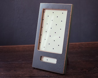 May include: A dark green picture frame with a white background and black polka dots. The frame has a small opening at the bottom for a note or a small photo.