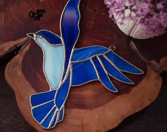 Könnte beinhalten: Ein blauer Glasvogel mit hellblauem Körper und dunkelblauen Flügeln, auf einer Holzscheibe ausgestellt.