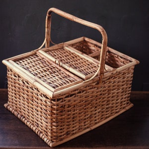 May include: A brown wicker picnic basket with a hinged lid and a handle. The basket has a divided interior for storing food and drinks.